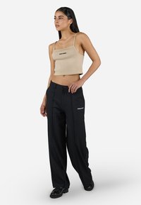 Beige ribbed crop top with thin straps, paired with loose black trousers featuring a logo and straight silhouette, worn with black shoes.