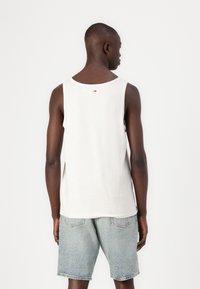 Top in cotone bianco senza maniche con scollatura rotonda, caratterizzato da un piccolo logo sul retro. Abbinato a pantaloni shorts in denim azzurro chiaro.