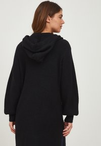 Schwarze gerippte Strickjacke mit Kapuze und langen Ärmeln, mit seitlichen Schlitzen und entspannter Passform. Weicher Stoff und lässiges Design.