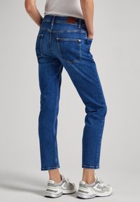 Blå denimjeans med rak ben-design, fem fickor och en brun läderlapp på midjan, i kombination med grå sneakers.