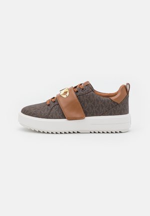 Brun mønstret sneaker med tan læderrem og accenter, hvid tyk sål med rillede bund og guld dekorativ hardware på rem.