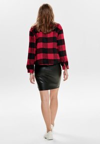 Chemise en flanelle à carreaux rouges et noirs, coupe courte, manches longues, associée à une mini-jupe en cuir noire et des baskets blanches.