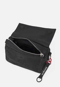 Borsa nera texture con chiusura a zip, design floreale a sbalzo e tracolla regolabile con un accento rosso e etichetta con il marchio.