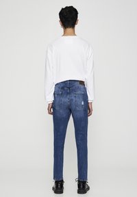 Camisa blanca de manga larga y jeans de mezclilla azules, con un corte recto, áreas deslavadas y dos bolsillos traseros. Zapatos negros completan el conjunto.