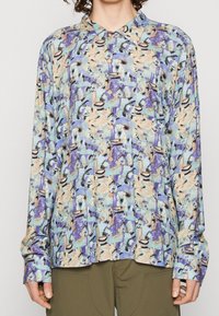 Camisa de manga larga con un patrón abstracto en azul claro, tonos terrenales y acentos en negro; con cierre de botones en la parte delantera y cuello clásico.