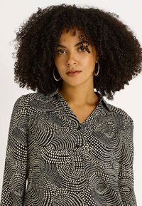 Blusa con estampado en blanco y negro, escote en V, mangas largas y tela texturizada que muestra formas geométricas en espiral.