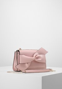 Różowa skórzana torebka na ramię z dużą kokardą z przodu, charakteryzująca się złotym łańcuchem i gładką teksturą, prostokątny kształt.