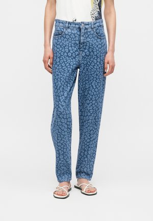 Lige blå jeans med mørkt leopardmønster, båret med hvide sandaler med stropper og en hvid top.