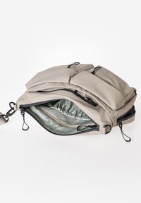 Beige gepolsterte Tasche mit Reißverschlussfächern, ausgestattet mit schwarzem Zubehör, glatter Textur und weicher Innenausstattung. Enthält Befestigungsschlaufen.