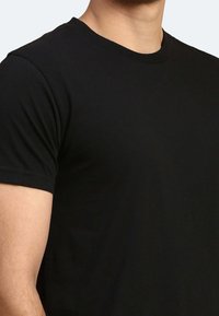 Maglietta nera con collo a giro e maniche corte. Realizzata in un tessuto liscio e leggero. Forma aderente, design minimalista.