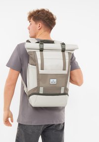 Világosszürke és olíva zöld roll-top hátizsák, állítható pántokkal, hálós zsebbel és logó címkével a hátoldalon. Tartós anyag.