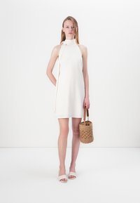 Baltas halter kleita ar gludu tekstūru, kurai ir sānu šķelumi. Modelis tur aušanas salmu somu ar cilindrisku formu un ādas siksnām.