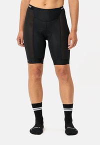 Pantaloni da ciclismo neri con pannelli laterali in mesh, dotati di un fondello imbottito per il comfort. Indossati con calzini neri con strisce bianche.