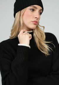 Pull noir en maille avec texture côtelée et bordure ivoire au col et aux poignets, assorti d'un bonnet noir assorti.