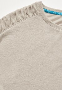 T-shirt in cotone color beige chiaro con finitura testurizzata, scollatura arricciata e un'etichetta a motivi blu a contrasto all'interno del colletto.