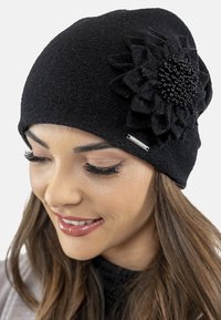 Bonnet en tricot noir avec un grand accent floral noir comportant des pétales en tissu et un centre perlé. Inclut un détail de logo métallique sur le côté.