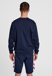 Marineblauwe sweatshirt met ribbels aan de boorden en onderkant; gedragen met marineblauwe shorts met rode, witte en blauwe zijstrepen. Zachte stof, ontspannen pasvorm.