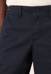 Pantalon en coton bleu marine avec une coupe standard. Les détails incluent des poches avant, une fermeture à bouton et des accents de couture discrets.