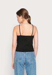 Top de alças finas, preto com textura canelada, de design justo, combinado com jeans de cintura alta, azul-claro, com bolsos traseiros.