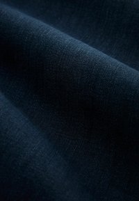 Tissu en denim bleu foncé avec un tissage serré visible et une texture douce, présenté en gros plan avec des plis et des ombres délicats.