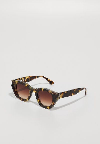 Tortoiseshell sunglasses featuring a bold geometric frame, gradient brown lenses, and wide, pointed arms with subtle branding detail.