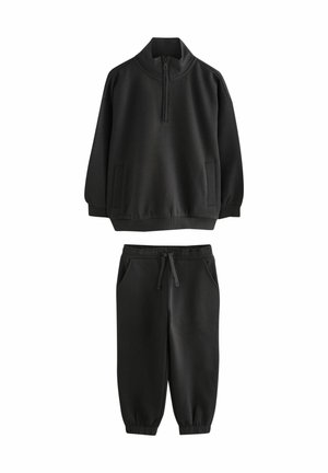 Felpa nera con colletto alto e mezza zip, abbinata a pantaloni jogger neri con vita elasticizzata e tasche laterali. Tessuto morbido e liscio.