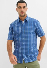 Camicia a maniche corte a quadretti blu con linee bianche a griglia, colletto classico, chiusura con bottoni e orlo piatto. Realizzata in cotone leggero.