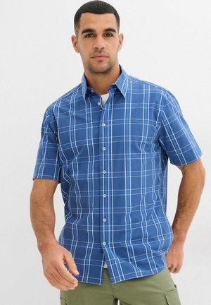 Camicia a maniche corte a quadretti blu con linee bianche a griglia, colletto classico, chiusura con bottoni e orlo piatto. Realizzata in cotone leggero.