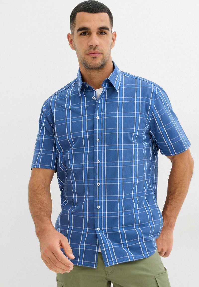 Camicia a maniche corte a quadretti blu con linee bianche a griglia, colletto classico, chiusura con bottoni e orlo piatto. Realizzata in cotone leggero.