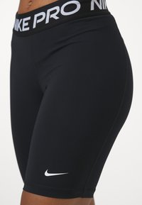 Crne Nike Pro atletske kratke hlače s bijelim logotipom, koje imaju uski kroj, meku tkaninu i elastični pojas za potporu.
