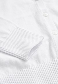 Cardigan blanc en maille avec poignets et ourlet côtelés, doté de boutons blancs le long de l'ouverture avant.