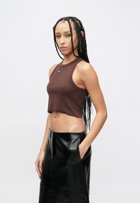 Καφέ ριμπ κοντό τοπ με στρογγυλή λαιμόκοψη και φαρδιές τιράντες, σε συνδυασμό με μαύρη δερμάτινη φούστα ψηλόμεση με πλαϊνές τσέπες.