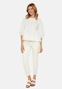 Top bianco a peplo con maniche a palloncino, abbinato a pantaloni bianchi aderenti e sandali bianchi con cinturini. Tessuto morbido, design semplice.