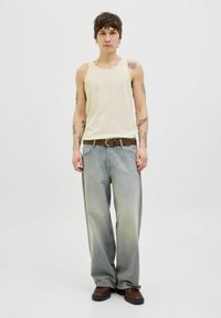 Maglietta canotta a righe gialla chiara, jeans larghi blu chiaro con leggere sfumature, cintura in pelle marrone e scarpe chunky marroni scure.