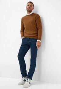 Maglione marrone a girocollo, jeans blu e sneakers bianche con dettagli navy. La vestibilità è casual, con un design semplice e un tessuto testurizzato.