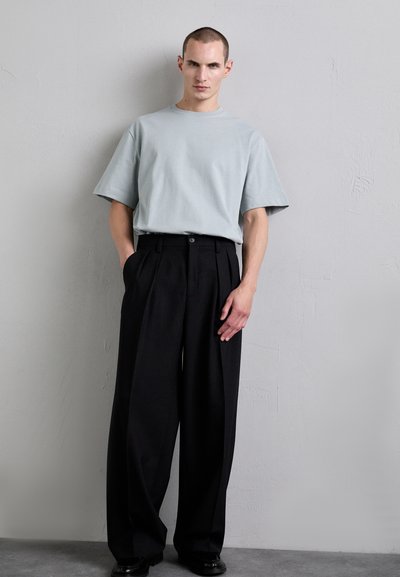 T-shirt oversize bleu clair à manches courtes, associé à un pantalon plissé noir, avec une fermeture à boutons et une coupe décontractée.