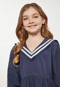 Navyblaues Kleid mit ausgestelltem Design, das einen tiefen V-Ausschnitt und weiße gestreifte Matrosenkragen-Akzente aufweist. Glatter Stoff mit gerafftem Taillenbereich.