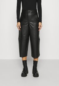 Svarta läderculotter med hög midja, med en mjuk textur och detaljerade framfickor, kombinerade med svarta snörstövlar.