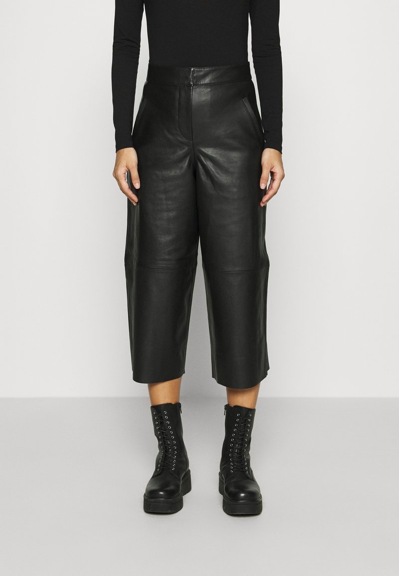 Svarta läderculotter med hög midja, med en mjuk textur och detaljerade framfickor, kombinerade med svarta snörstövlar.