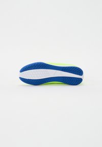 Suela de zapato con una base verde neón brillante, patrones de tracción azules, media suela blanca y elementos texturizados para mayor agarre.