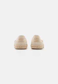 Beige Baumwollslippers mit gewebter Textur, Jutebesatz und einem Patchdetail an der Seite. Rundes Rückendesign.