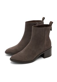 Stivali alla caviglia in suede marrone con punta appuntita, chiusura con zip su un lato e tacco a blocco. Presentano una linguetta per un facile indossamento.