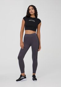 Czarny krótki t-shirt z nadrukiem "NEW YORK", w zestawieniu z szarymi legginsami o wysokim stanie z bocznymi akcentami oraz czarnymi butami sportowymi.