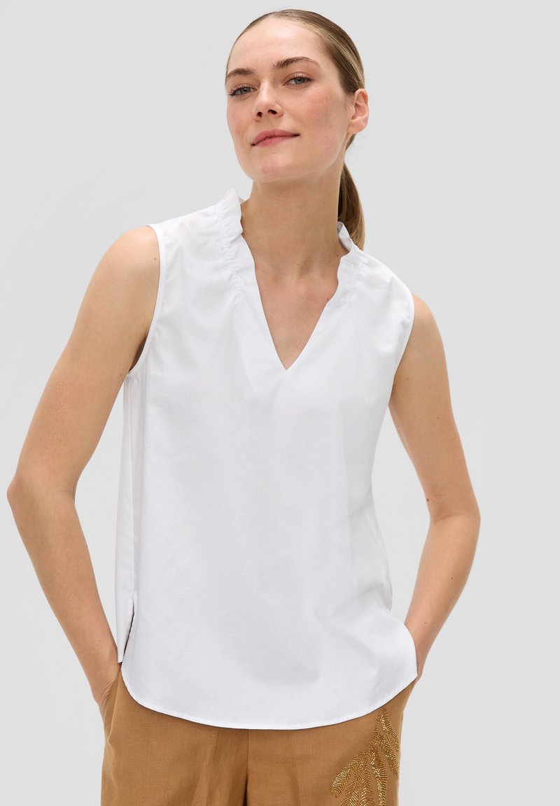 Biała bezrękawnikowa bluzka z falbaniastym dekoltem i wycięciem w kształcie litery V. Wykonana z gładkiego materiału, z bocznymi rozporkami dla luźniejszego kroju.