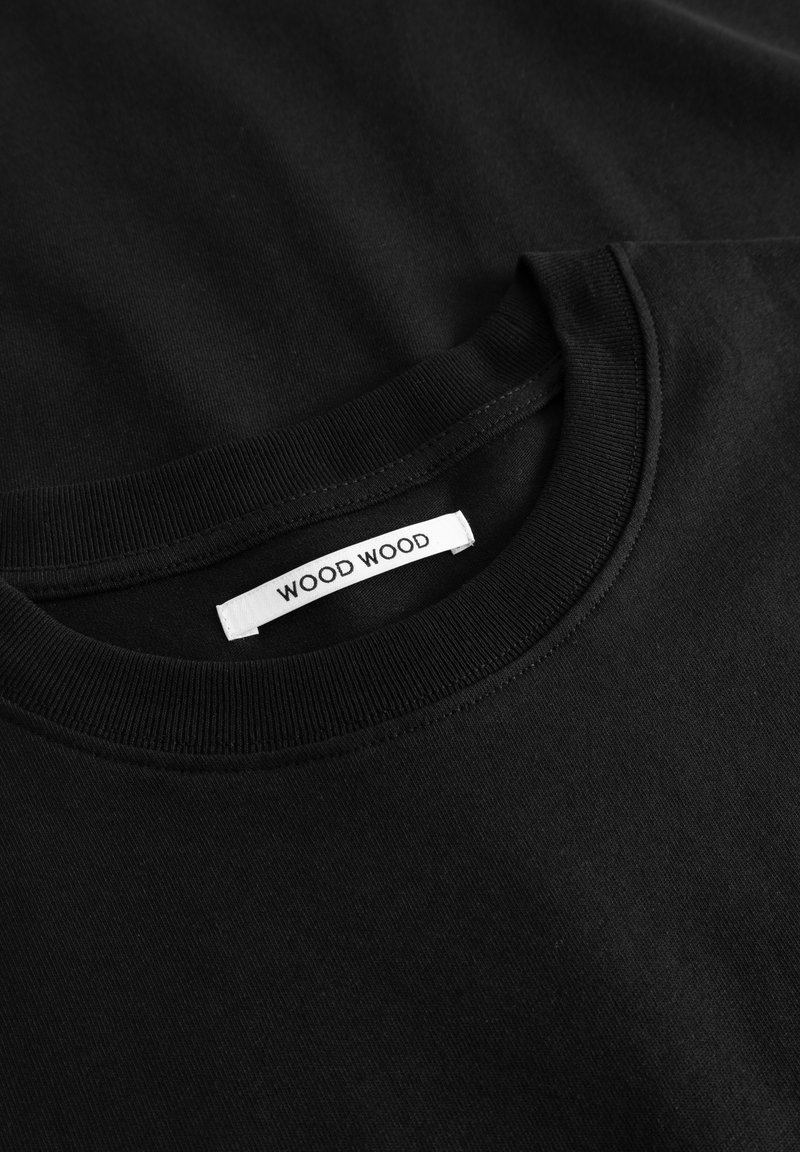 Schwarzes Baumwoll-T-Shirt mit Rundhalsausschnitt, featuring einer gerippten Kragen und einem weißen Stoffetikett mit der Aufschrift "WOOD WOOD" in Schwarz.