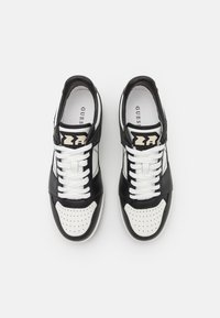 Sneaker in pelle bianca e nera con punta perforata, lacci bianchi piatti e dettagli del logo sulla linguetta. Superfici lisce e testurizzate.