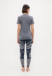 Une chemise grise à manches courtes associée à des leggings texturés et à motifs avec des rayures bleu marine, grises et blanches, ainsi que des motifs géométriques dans le dos.