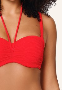 Červený bandeau bikiny top s textúrovanou tkaninou a tenkými nastaviteľnými ramienkami; obsahuje skladané detaily v strede a bezšvový dizajn.