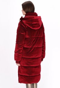 Vörös bélelt kabát kapucnival, bordázott, texturált anyagból. A fazon hosszú ujjú és térdig érő szabású.