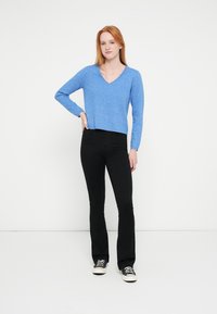 Zils, garām piedurknēm, V veida kakla džemperis ar īsu dizainu, kombinēts ar melnām zvīņainām biksēm un baltām sporta kurpēm. Gluda tekstūra, ikdienišķs piegriezums.